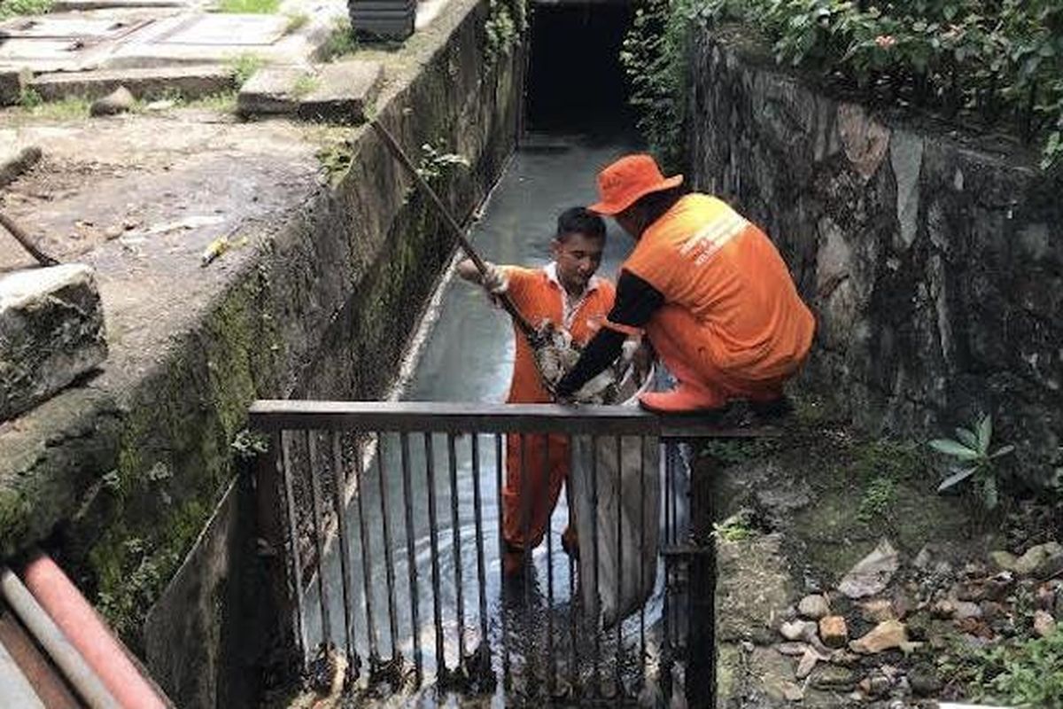 Petugas PPSU sedang membersihkan selokan dari berbagai sampah. 