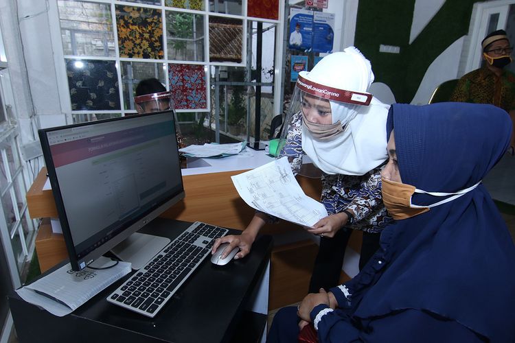 Petugas menggunakan penutup wajah (face shield) ketika memberikan layanan dokumen kependudukan kepada warga di Kantor Desa Genteng Wetan, Banyuwangi, Kamis (28/5/2020). Kantor Desa Genteng Wetan menjadi salah satu proyek percontohan persiapan penerapan normal baru di Kabupaten Banyuwangi.