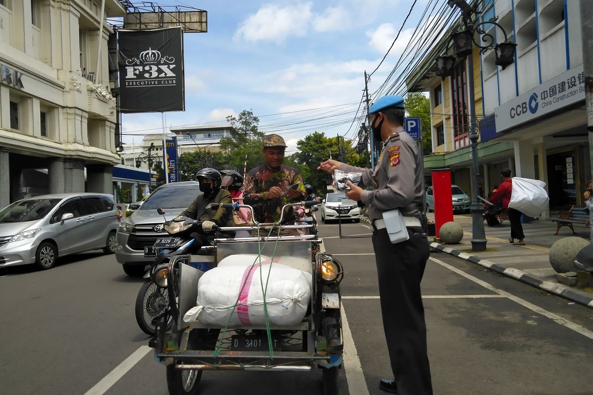 Polisi tengah membagikan masker kepada pengendara dan warga sekitar sekaligus menyosialisasikan PPKM berbasis mikro.