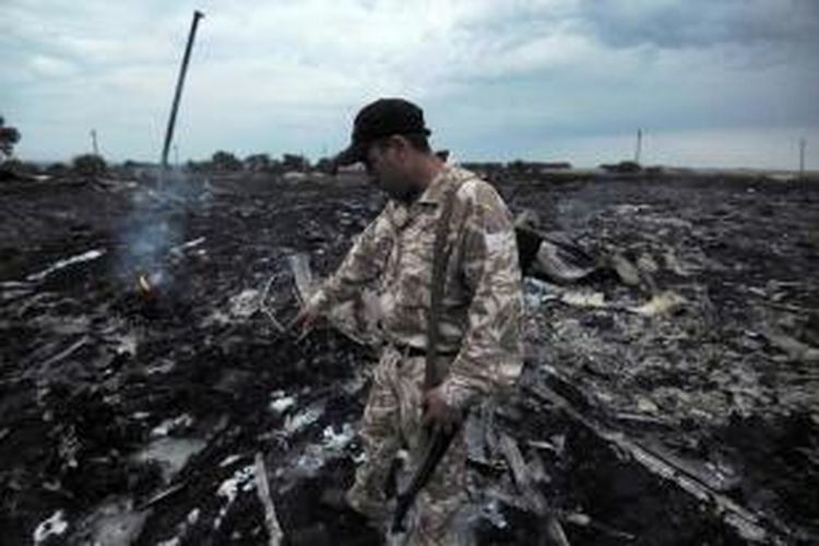 Seorang pria mengenakan seragam militer berada di dekat puing pesawat Malaysia Airlines yang membawa 295 orang penumpang dari Amsterdam ke Kuala Lumpur yang jatuh di Kota Shaktarsk, timur Ukraina, Kamis (17/8/2014).