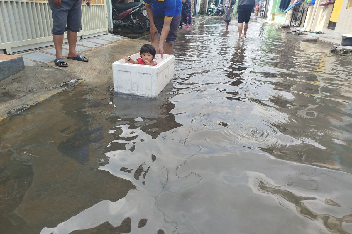 Seorang anak bermain air saat banjir rob. Ia menggunakan kotak sterofoam sebagai perahu di Kelurahan Pangeranan, Kabupaten Bangkalan, Jumat (30/5/2025). 