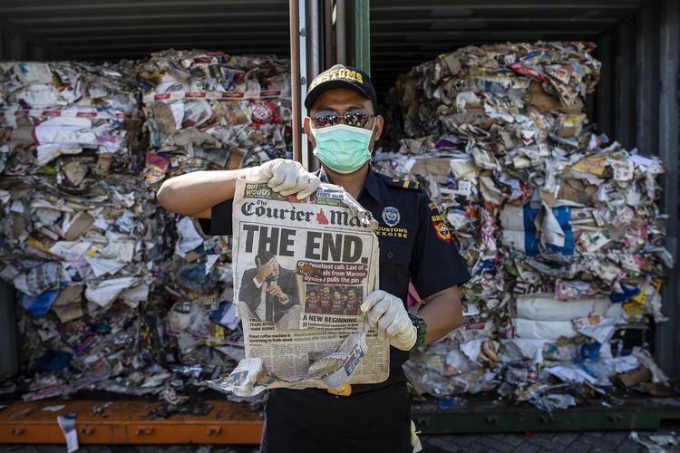 Seorang petugas bea cuka memegang selembar harian di kontainer berisi sampah yang berasal dari Australia. Sampah itu tak hanya berisi kertas. Namun juga sampah plastik saat dilakukan pemeriksaan di Surabaya pada 9 Juli 2019.