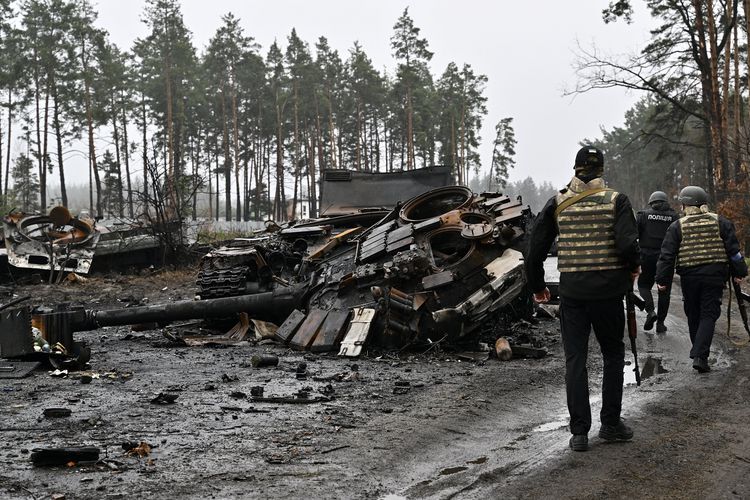 Polisi Ukraina berjalan melewati puing-puing tank Rusia dan peralatan personel yang hancur di desa Dmytrivka, Kyiv barat, 2 April 2022.