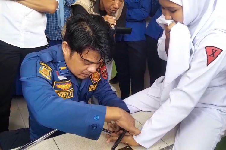 TERJEPIT—Salah satu petugas Damkar Pemkab Ngawi berusaha mengeluarkan jari telunjuk tangan kiri Najwa Asya, 16, siswi kelas 10 jurusan Asisten Keperawatan SMK BIM Ngawi yang terjepit kursi besi di ruang kelasnya, Rabu (24/9/2025).