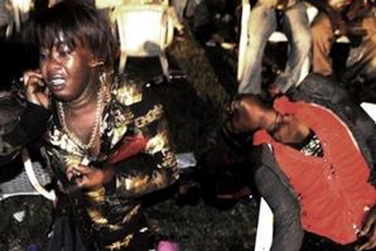 Seorang korban selamat duduk di sebelah saudaranya yang tewas setelah sebuah bom meledak di restoran Ethiopia, distrik Kabalagala, Kampala, Uganda, 11 Juli 2010. 