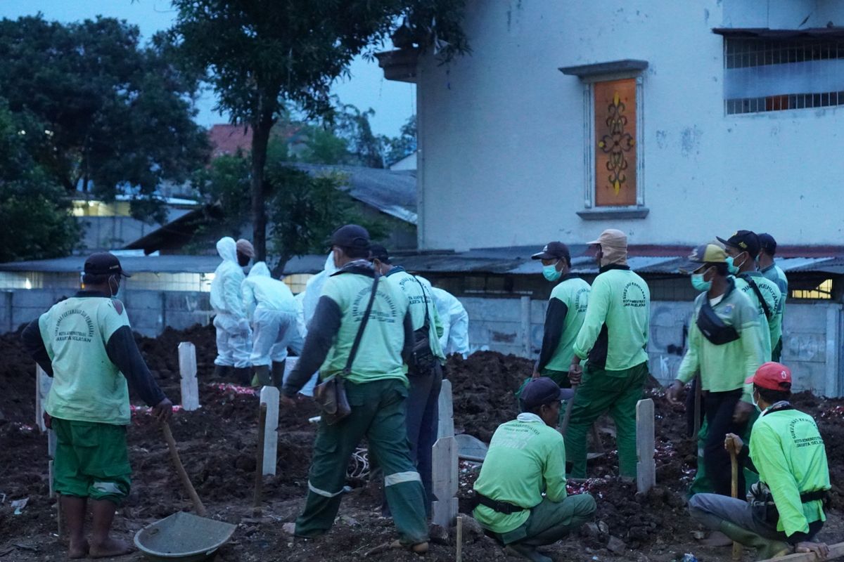 Para penggali kubur bersiap memakamkan peti jenazah pasien Covid-19 di Taman Pemakaman Umum (TPU) Srengseng Sawah, Jagakarsa, Jakarta Selatan pada Jumat (15/1/2021). TPU Srengseng Sawah dijadikan sebagai tempat pemakaman jenazah pasien Covid-19 sejak Selasa (12/1/2021). TPU Srengseng Sawah memiliki lahan seluas 0,5 hektar dan bisa menampung sekitar 700 makam untuk jenazah pasien Covid-19.