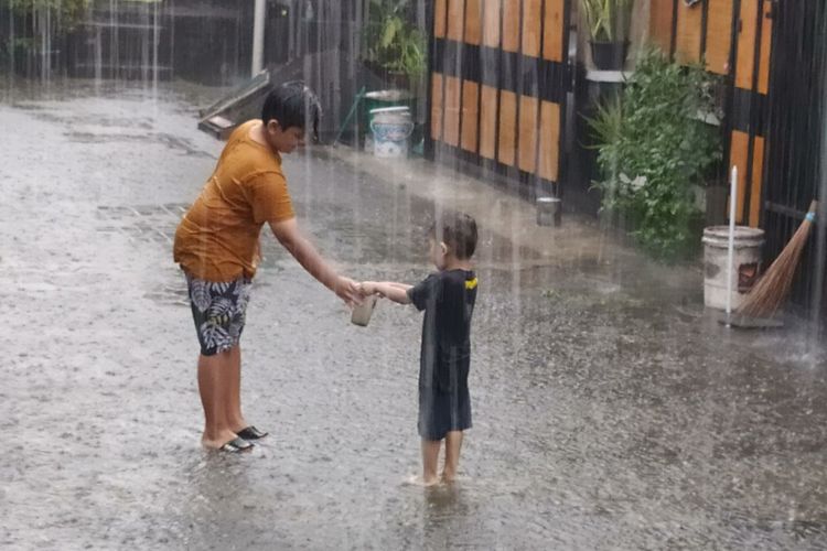 Dua anak sedang bermain hujan-hujanan.