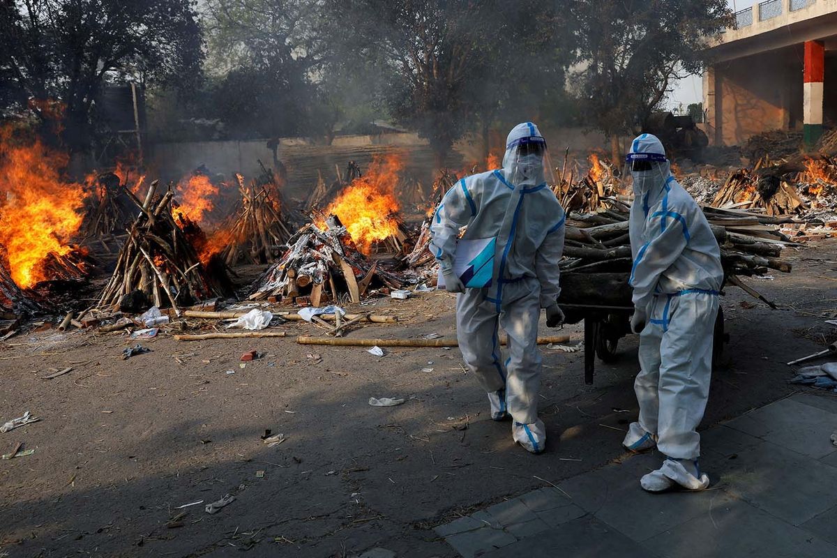 Petugas kesehatan yang mengenakan alat pelindung diri (APD) membawa kayu untuk menyiapkan tiang pemakaman untuk korban penyakit virus corona (COVID-19) selama kremasi massal di krematorium di New Delhi, India, Senin (26/4/2021).