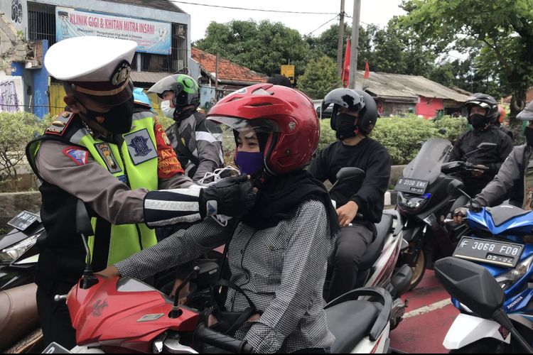 Anggota kepolisian membantu pengendara memasang tali pengikat helm di persimpangan Jalan Siliwangi, Pancoran Mas, Depok pada Senin (15/11/2021) pagi.