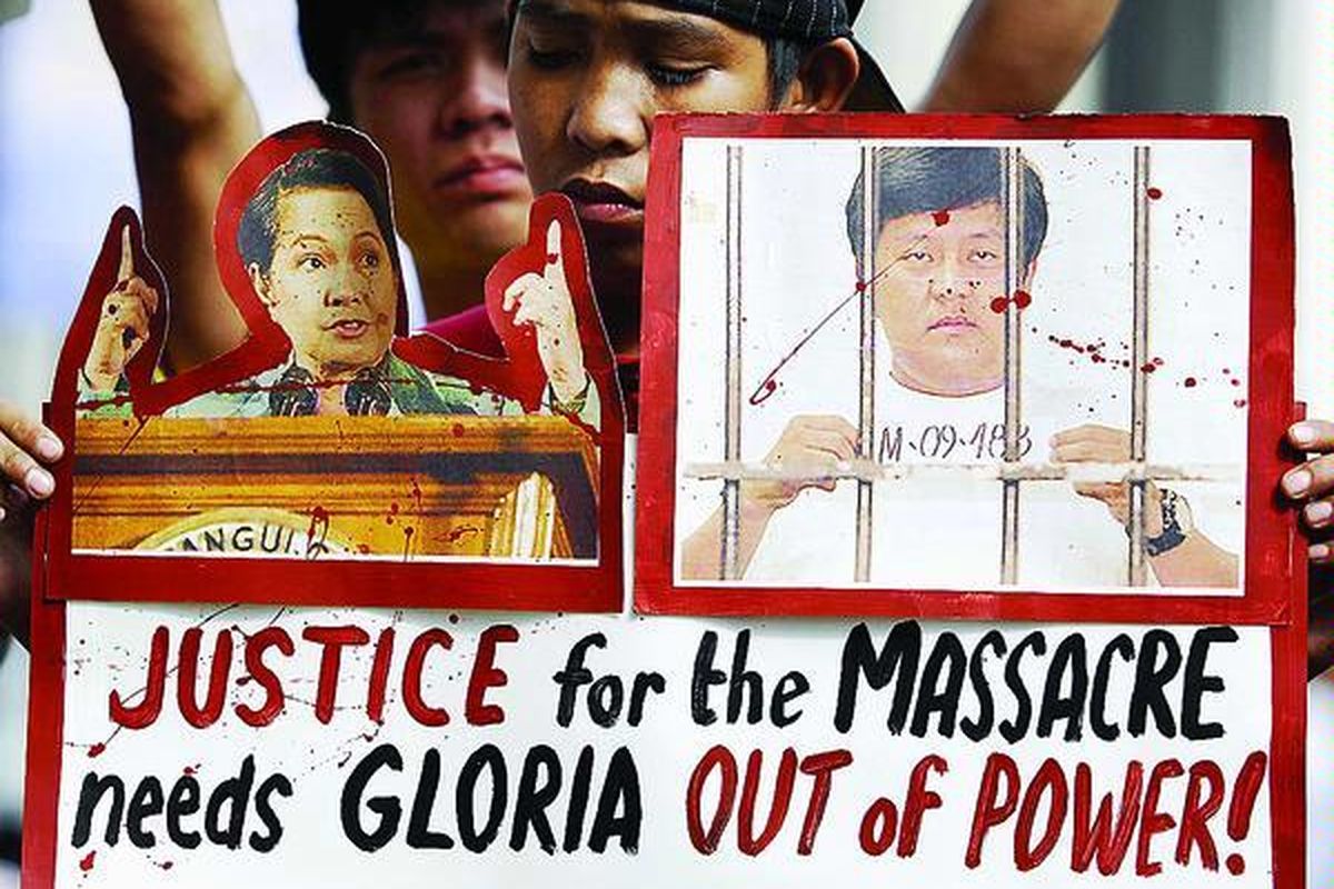 Seorang aktivis antipemerintah membawa plakat di depan gedung Komisi Pemilu (Comelec) di Manila, Selasa (1/12). Selain membawa gambar Presiden Filipina Gloria Macapagal-Arroyo (kiri) yang mereka tuntut untuk mundur, para aktivis juga memprotes Wali Kota Maguindanao, yang dituduh berada di belakang aksi pembantaian bermotif politik di Filipina selatan pekan lalu.