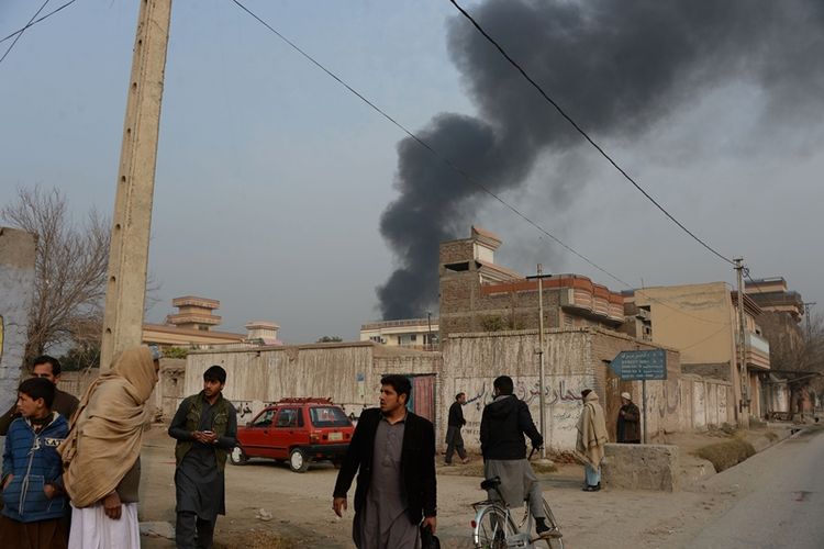 Warga sipil Afghanistan berkumpul di sebuah jalan, di samping gedung yang mengeluarkan kepulan asap, sekitar kantor amal berbasis di Inggris, Save the Children, dalam serangan yang sedang berlangsung di Jalalabad, Afghanistan, Rabu (24/1/2018). (AFP/Noorullah Shirzada)