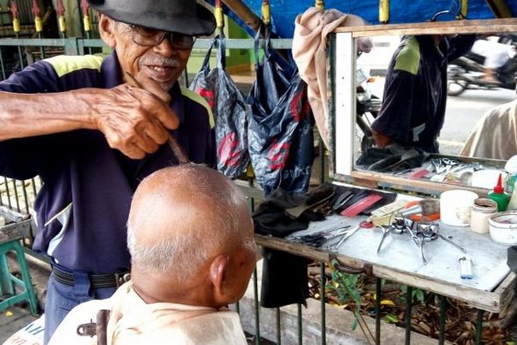 Mbah Nartowiono tukang cukur yang pinggir alun-alun Utara  Yogyakarta saat melayani pelanggannya.