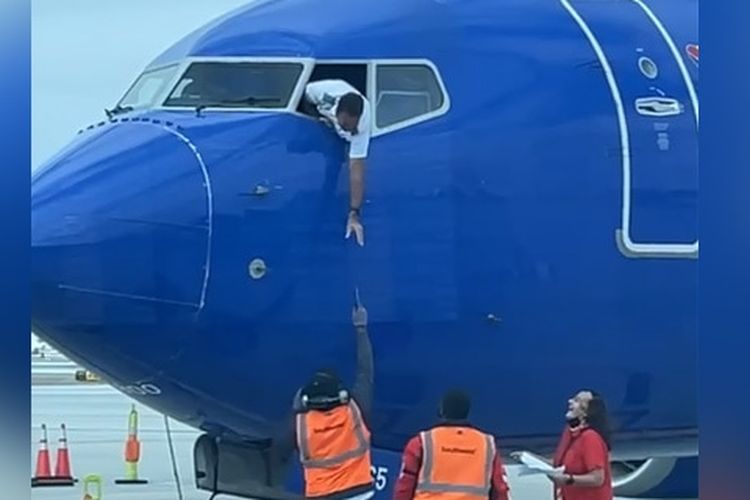 Pilot menjulurkan tubuh meraih ponsel penumpang.