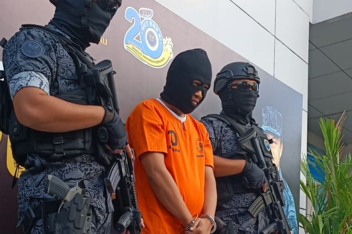 Buronan kasus skimming Mabes Polri berinisial MI, dikawal petugas bersenjata saat dihadirkan dalam rilis pengungkapan kasus Narkotika di BNNP Bali pada Jumat (5/7/2022). Kompas.com/ Yohanes Valdi Seriang Ginta