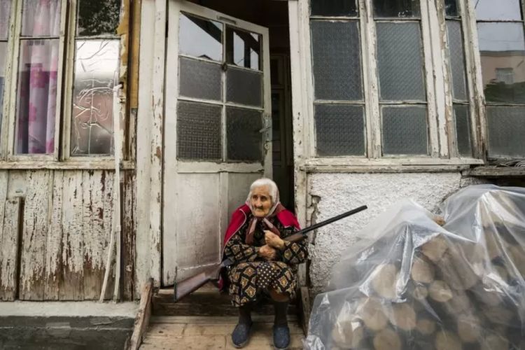 Seorang perempuan lansia berjaga di depan rumah di kota Stepanakert dengan senjata di tangannya.