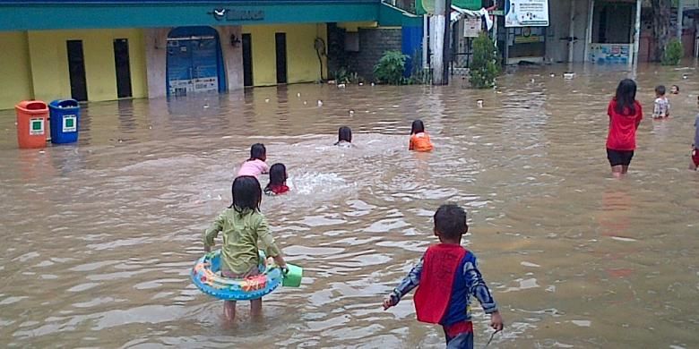 Anak-anak bermain di genangan air depan selter transJakarta Bidara Cina, Jakarta Timur, Minggu (19/1/2014).