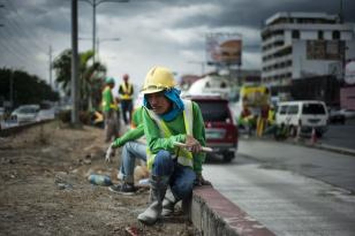 Pekerja meletakkan beton pada bagian dari sebuah jalan raya utama di Manila.