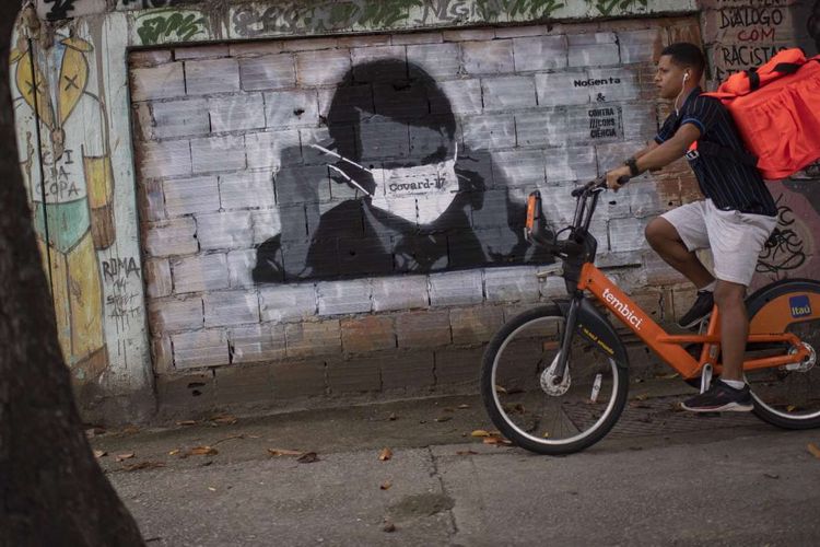 Seorang warga bersepeda melintas di depan gambar mural Presiden Brazil Jair Bolsonaro di Rio de Janeiro, Brazil, 24 Maret 2020. Pandemi Covid-19 yang disebabkan oleh virus corona menjadi insipirasi seniman grafiti untuk memberikan peringatan dan motivasi bagi warga dalam menghadapi virus tersebut.