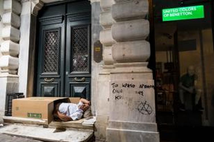 Seorang pria tunawisma tidur berselimutkan kardus di pelataran sebuah toko yang tutup di pusat kota Athena, Yunani.