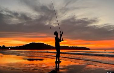 Seorang anak laki-laki memancing saat matahari terbenam di Pantai Bang Tao di Phuket, Thailand, 6 Desember 2021.