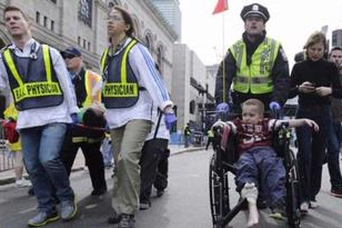 Seorang polisi Boston mendorong kursi roda yang membawa seorang anak yang terluka di Boylston Street. Di sampingnya sejumlah petugas medis membawa pelari yang terluka