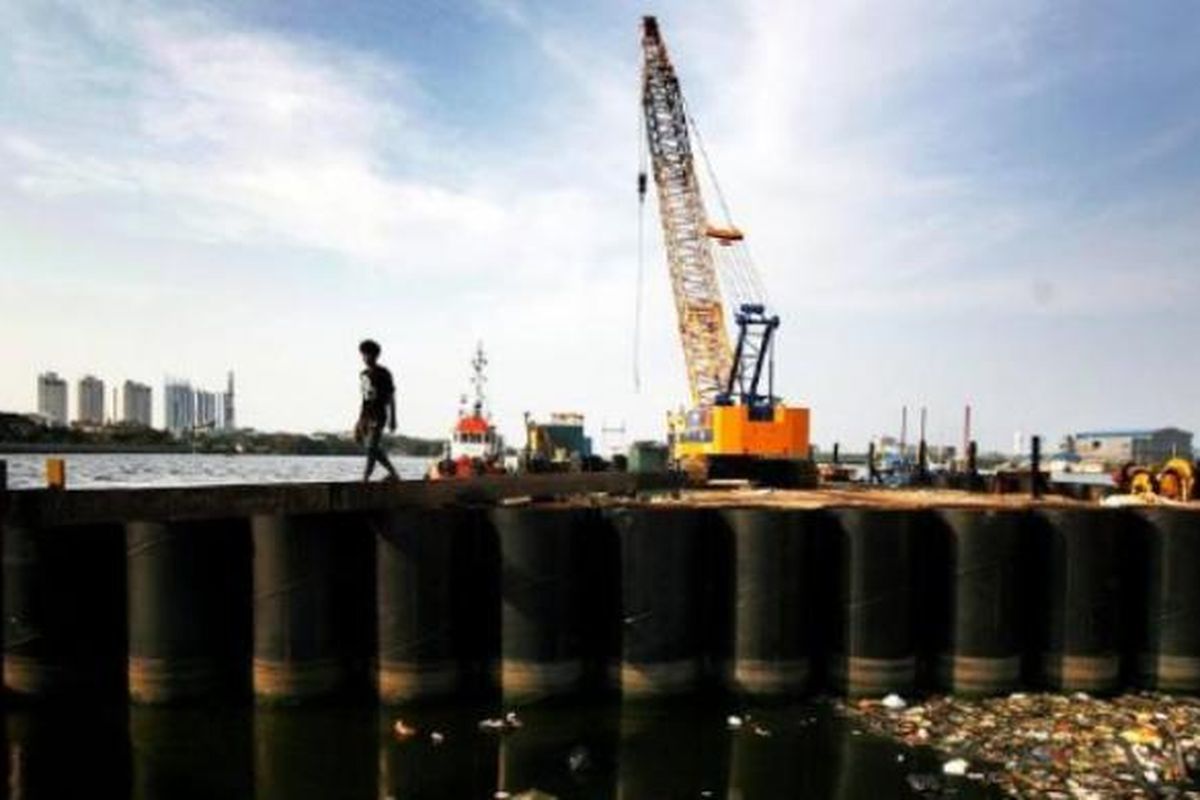 Warga melintas di antara dinding tabung raksasa yang dipasang sebagai bagian dari proyek pembangunan tanggul laut raksasa di Jakarta Utara, November 2014. 