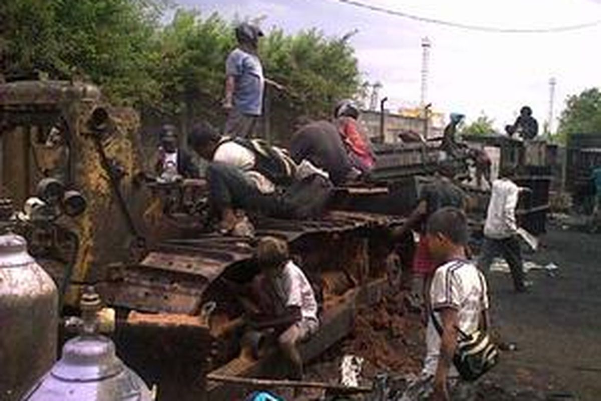 Warga Koja sibuk mempreteli bagian dari bangkai mobil yang masih tersisa di jalan akses menuju Makam Mbah Priok, Jumat (16/4/2010).