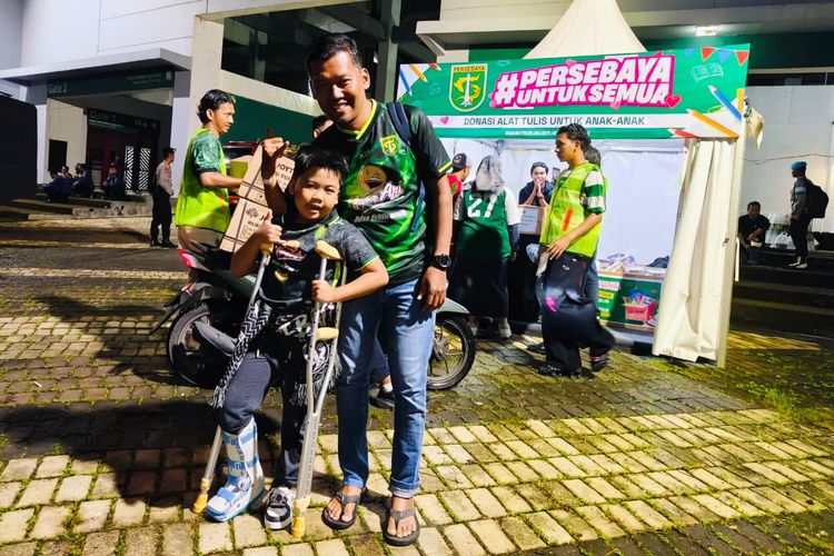 Seorang suporter bersama anaknya foto di depan booth setelah menyerahkan donasi alat tulis sebelum laga pekan ke-21 Super League 2025-2026 Persebaya mealwan Bhayangkara Presisi Lampung FC di Stadion Gelora Bung Tomo Surabaya, Jawa Timur, Sabtu (14/2/2026) malam, untuk membantu anak-anak yang membutuhkan.