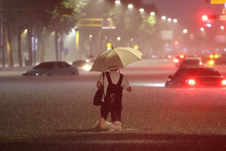 Seorang pria mengarungi mobil yang terendam air di jalan saat hujan deras di distrik Gangnam, Seoul pada 8 Agustus 2022.