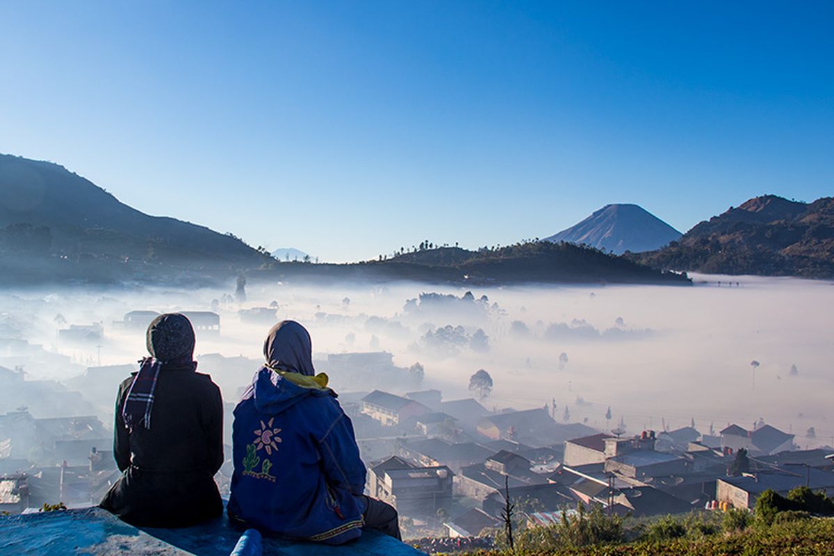 Dua wanita menikmati keindahan Dataran Tinggi Dieng yang berselimut kabut.