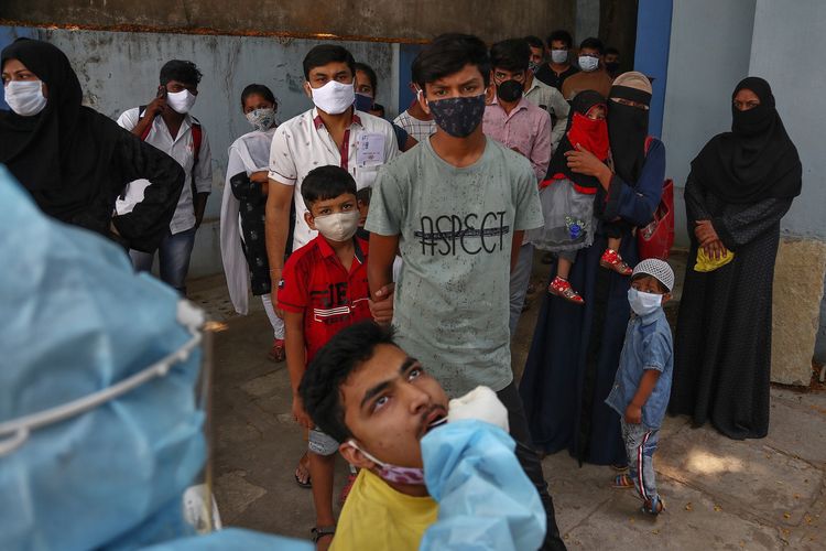 Petugas medis mengambil sampel dari swab mulut seorang pria muda yang tes Covid-19, sementara orang-orang lainnya mengantre giliran tes di sebuah rumah sakit Hyderabad, India, pada Senin (19/4/2021).