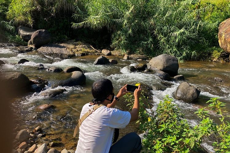 Seorang wisatawan sedang memotret sebuah bunga di aliran sungai di Kecamatan Babakan Madang, Kabupaten Bogor, Rabu (26/5/2021).