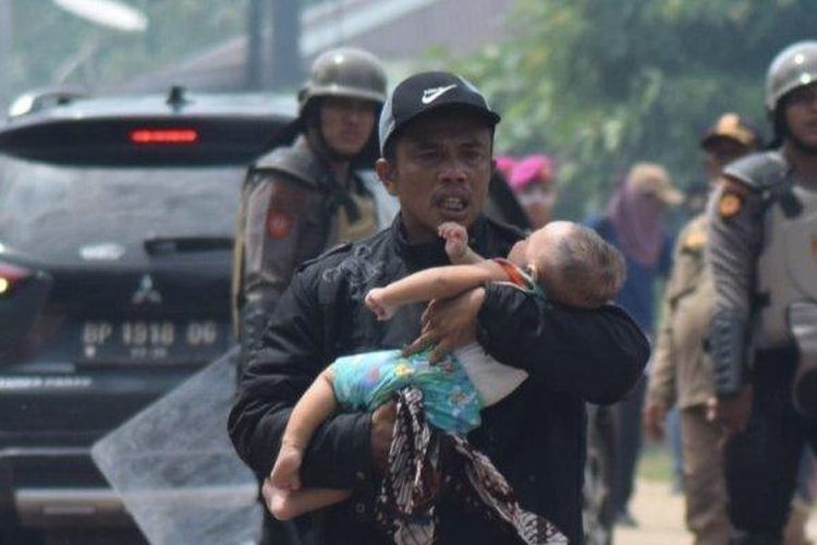 Herman menggendong bayinya yang pingsan di tengah bentrokan warga Rempang dan aparat gabungan di Jembatan 4 Barelang, Batam, Kamis (7/9/2023). Bayinya pingsan karena gas air mata masuk ke dalam rumahnya lewah jendela yang terbuka. 

