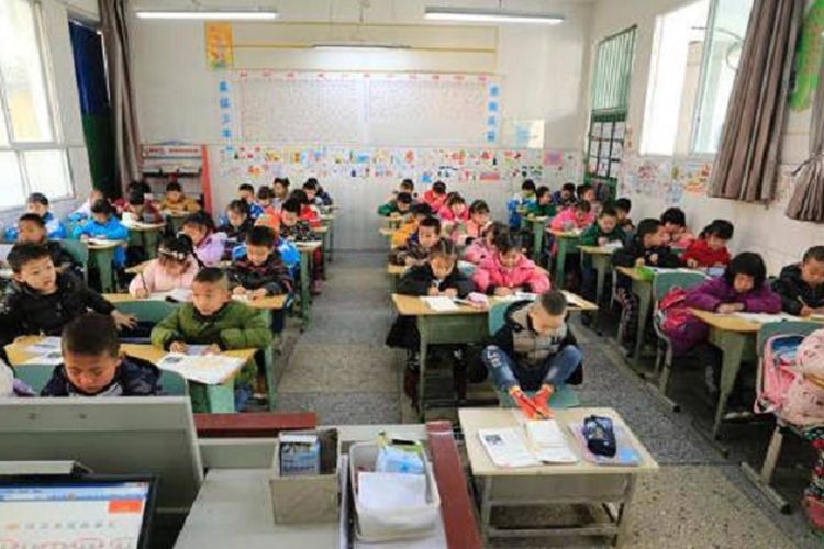 Jiang Tianjing (8) duduk di deret terdepan di dalam kelas.