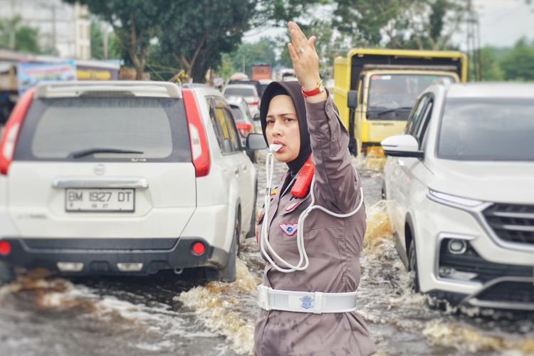 Kasatlantas Polres Rohil Iptu Zahratul Aulia Harun mengatur lalu lintas di jalan lintas sumatera yang terendam banjir di Kecamatan Tanah Putih, Kabupaten Rokan Hilir, Riau, Minggu (14/1/2024).