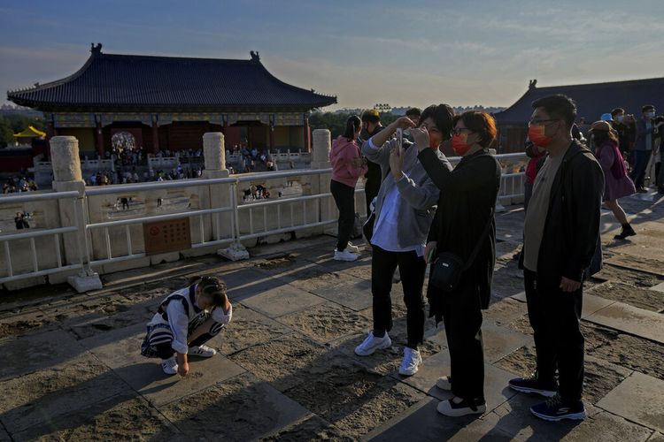 Seorang anak bereaksi saat kerabatnya melihat-lihat foto smartphone mereka saat pengunjung mengunjungi Kuil Surga pada hari terakhir Hari Nasional China selama seminggu di Beijing, Kamis, 7 Oktober 2021. 