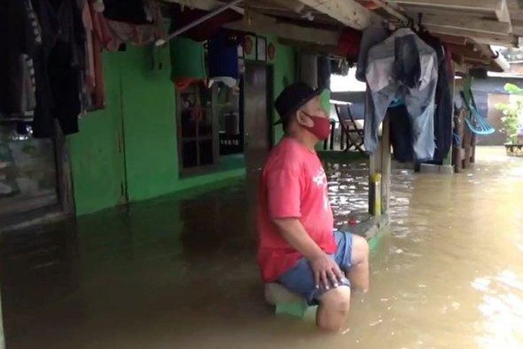 Permukiman di RT 001/03 Cipinang Melayu, Makasar, Jakarta Timur, Selasa (16/2/2021), terendam banjir. Seorang warga duduk di teras rumahnya di tengah banjir. 