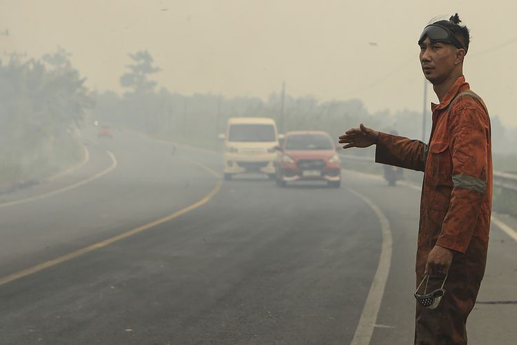 Petugas Badan Penanggulangan Bencana Daerah (BPBD) Sumatera Selatan mengatur lalulintas yang disleimuti kabut asap akibat kebakaran hutan dan lahan di jalan lintas Palembang-Ogan Ilir.