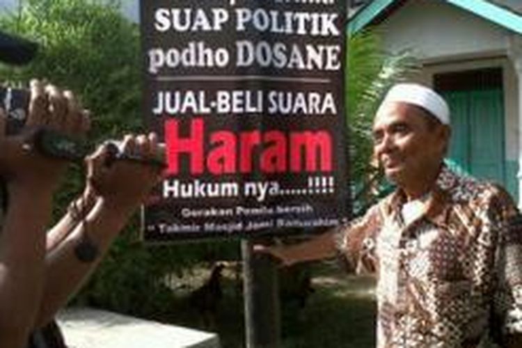 Salah seorang takmir Masjid Baiturrohim, Dusun Karang Harjan, Desa Gunungpring, Kecamatan Muntilan, Kabupaten Magelang, memasang banner pesan 