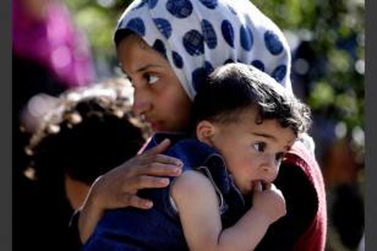 Seorang perempuan pengungsi Suriah membawa adiknya, saat ia mendengarkan Komisi Tinggi PBB untuk Pengungsi, UNHCR, Antonio Guterres kepala (tidak terlihat) berbicara selama kunjungannya ke kamp pengungsi Suriah, di Desa Ketermaya, tenggara Beirut, Lebanon, 14 Maret 2013.