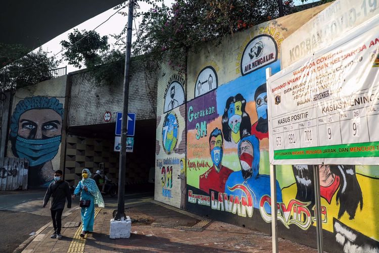 Warga saat melintasi mural berisi pesan ajakan menggunakan masker di Cikoko, Pancoran, Jakarta Selatan, Sabtu (3/10/2020). Pembatasan sosial berskala besar (PSBB) di Jakarta untuk mengendalikan penularan Covid-19 telah memasuki pekan ketiga.