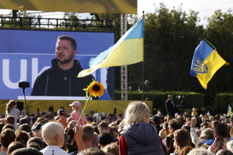 Anak-anak melihat ketika seorang anggota masyarakat memegang bunga matahari sementara Presiden Ukraina Volodymyr Zelensky berpidato di hadapan kerumunan orang di Lukiskiu Square di Vilnius pada 11 Juli 2023, selama KTT NATO. 