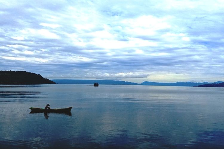 Seorang nelayan tradisional menebar jala di perairan Danau Toba yang bentang alamnya begitu indah