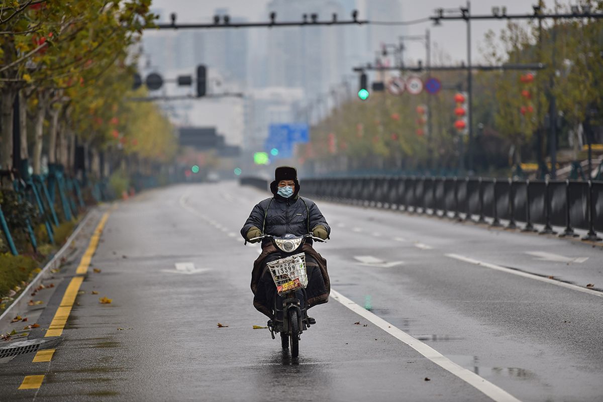 Seorang pria mengenakan masker saat mengendarai sepeda motor di jalanan kota Wuhan, China, yang sepi akibat wabah virus corona yang mematikan, Minggu (26/1/2020).