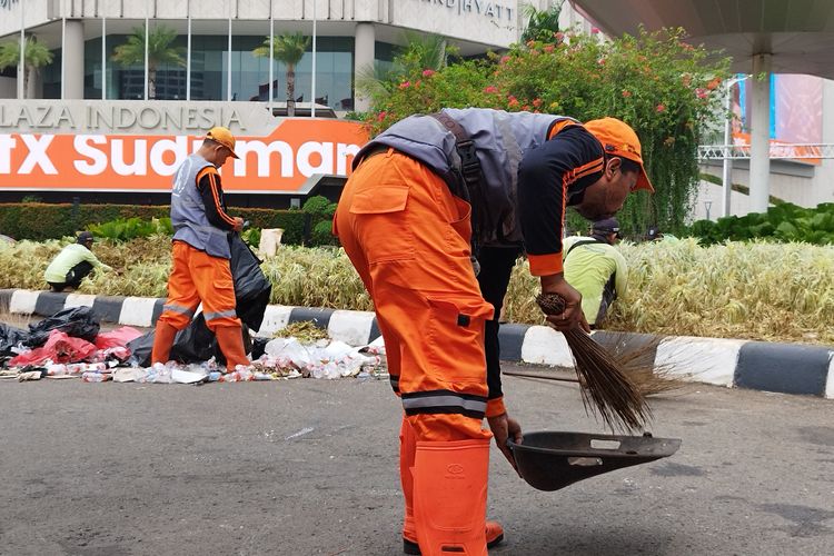 Pasukan oranye membersihkan sampah yang berserakan di Bundaran HI, Jakarta Pusat, Senin (1/1/2024).