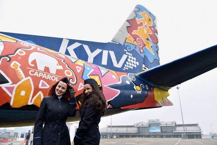 Pramugari maskapai Ukraina berpose di depan pesawat Antonov-24 yang dihiasi lukisan karya seniman Avtandil Gurgenidze di bandara internasional Zhulyany, November 2015.