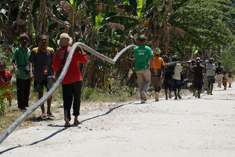 Warga Desa Nifukani bergotong royong mengangkut pipa transmisi air menembus medan berbukit untuk mengalirkan air bersih ke rumah-rumah warga. 