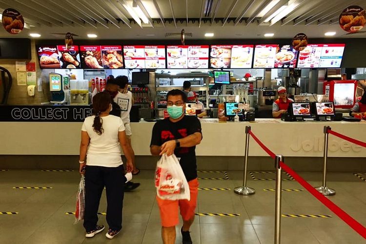 Seorang pembeli yang memakai masker meninggalkan gerai fast food Jollibee di Lucky Plaza, Orchard, Singapura setelah membeli makanannya, Sabtu siang (11/04/2020). Makanan yang dibeli harus disantap di kediaman masing-masing sejak kebijakan Circuit Breaker atau setengah lockdown diberlakukan di Singapura mulai Selasa (07/04/2020)