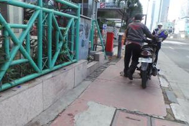 Pria ini terlihat mendorong motor di trotoar Jalan MH Thamrin, Jakarta Pusat, Rabu (17/12/2014). D jalur itu, sepeda motor dilarang melintas.