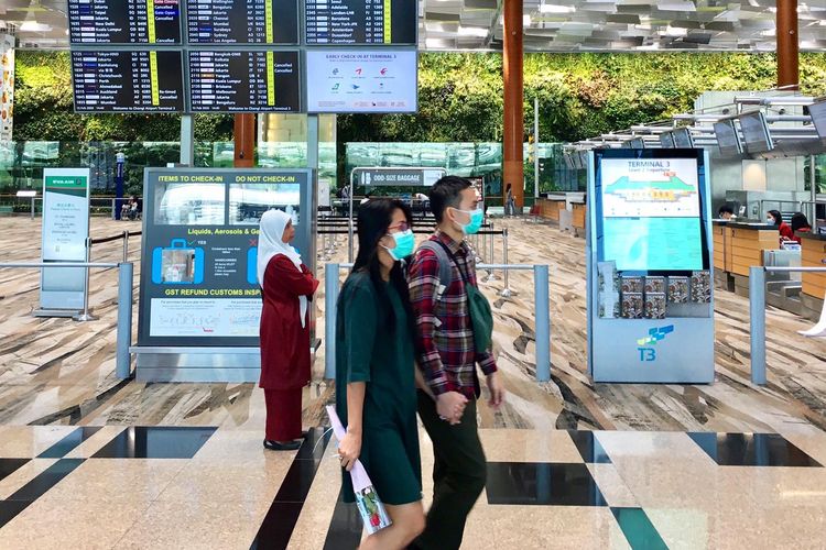 Pasangan muda-mudi terlihat memakai masker di Bandara Internasional Changi di tengah mewabahnya virus corona di Singapura.